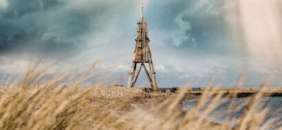 Das Wahrzeichen Kugelbake ragt als hölzernes Seezeichen an der Küste von Cuxhaven empor.