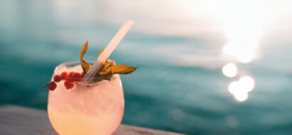 Ein erfrischender Cocktail steht am Wasser und fängt die Abendsonne ein.